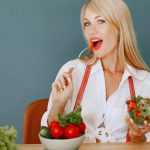 Woman enjoying a fresh salad with tomatoes and greens, promoting healthy eating.